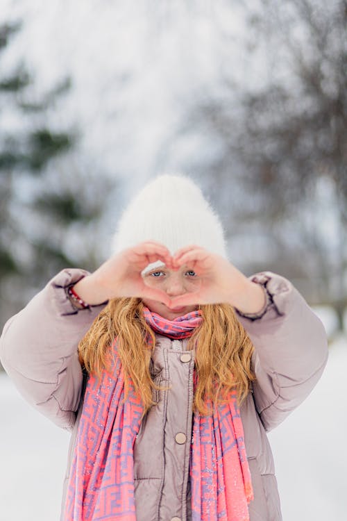Free A girl in a winter hat making a heart shape with her hands Stock Photo