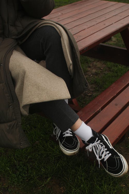 Legs of Person Wearing Vans Sneakers and Sitting on Wooden Bench