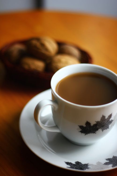 Free Warm coffee in a maple leaf-designed cup on a fall morning, with walnuts in the background. Stock Photo