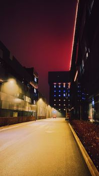 A deserted city street at night with illuminated buildings and a striking red sky.