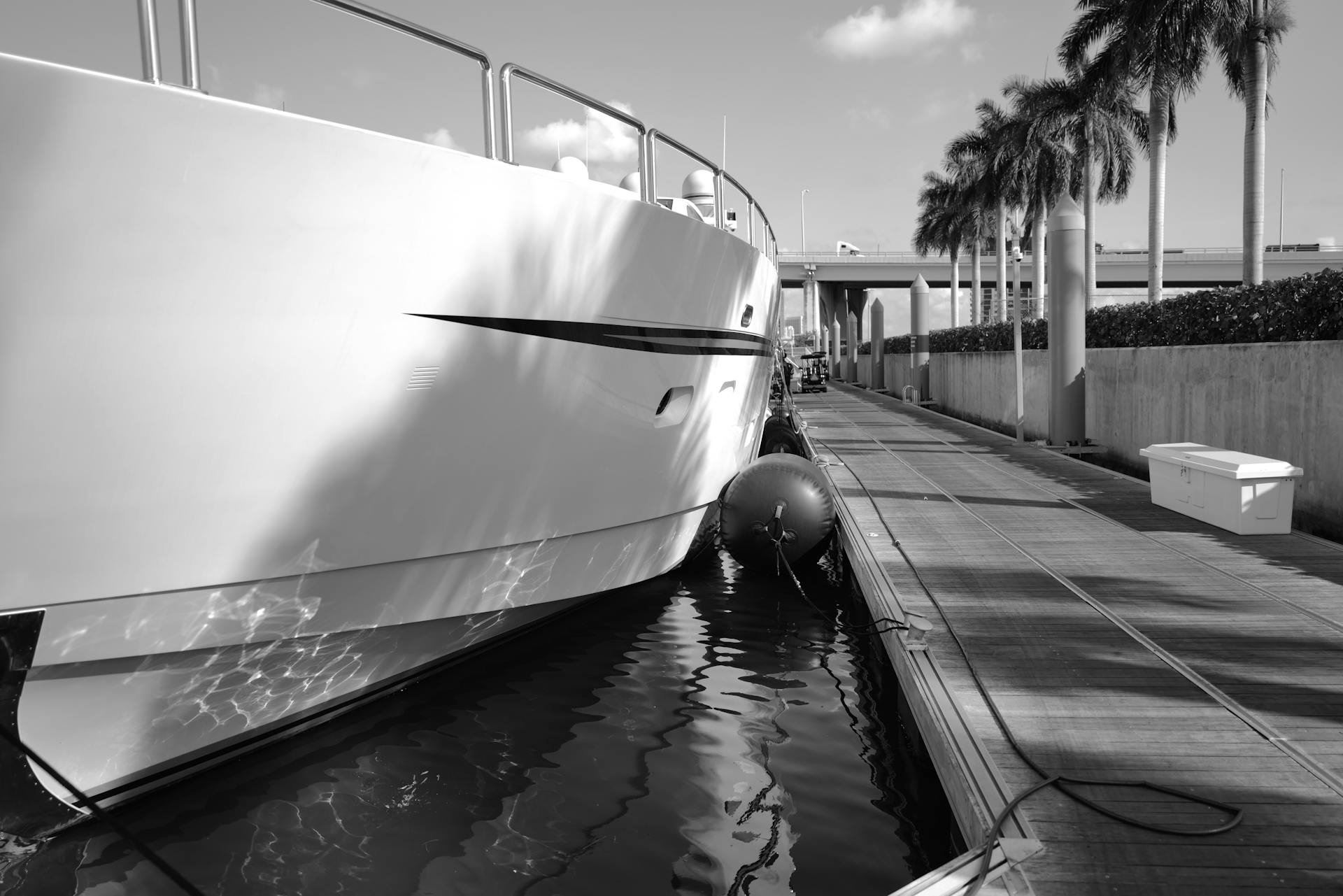 A luxurious yacht moored in Miami's marina, captured in black and white with palm trees swaying nearby.