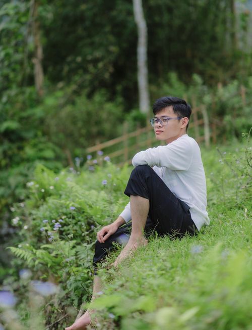 Free Young man in eyeglasses sitting in a verdant meadow contemplating nature. Stock Photo