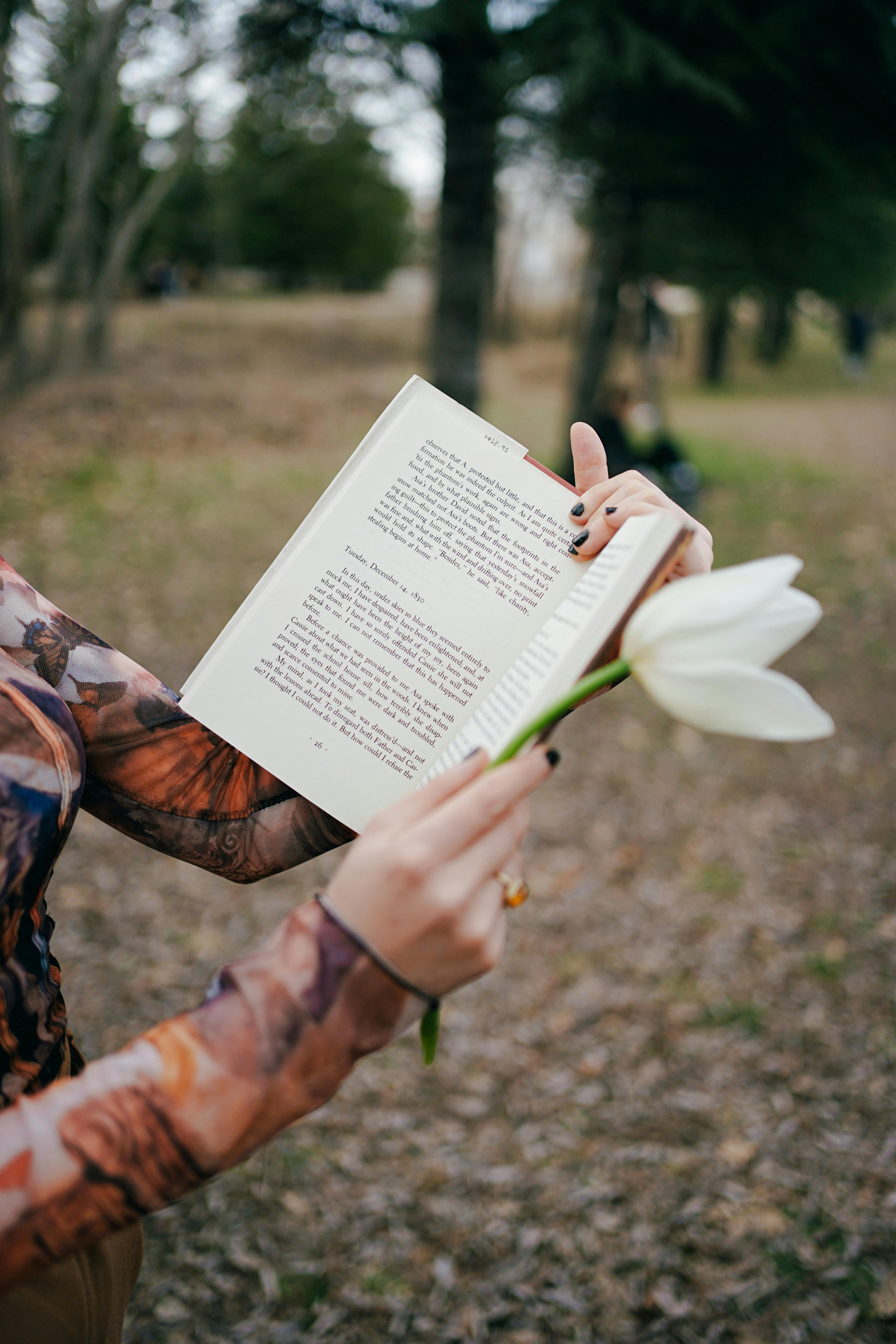 A woman holds a book and white flower, enjoying a peaceful day in an Ankara park.