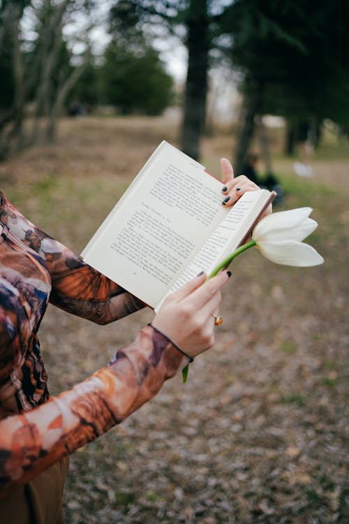 A woman holding a book and flowers in the woods