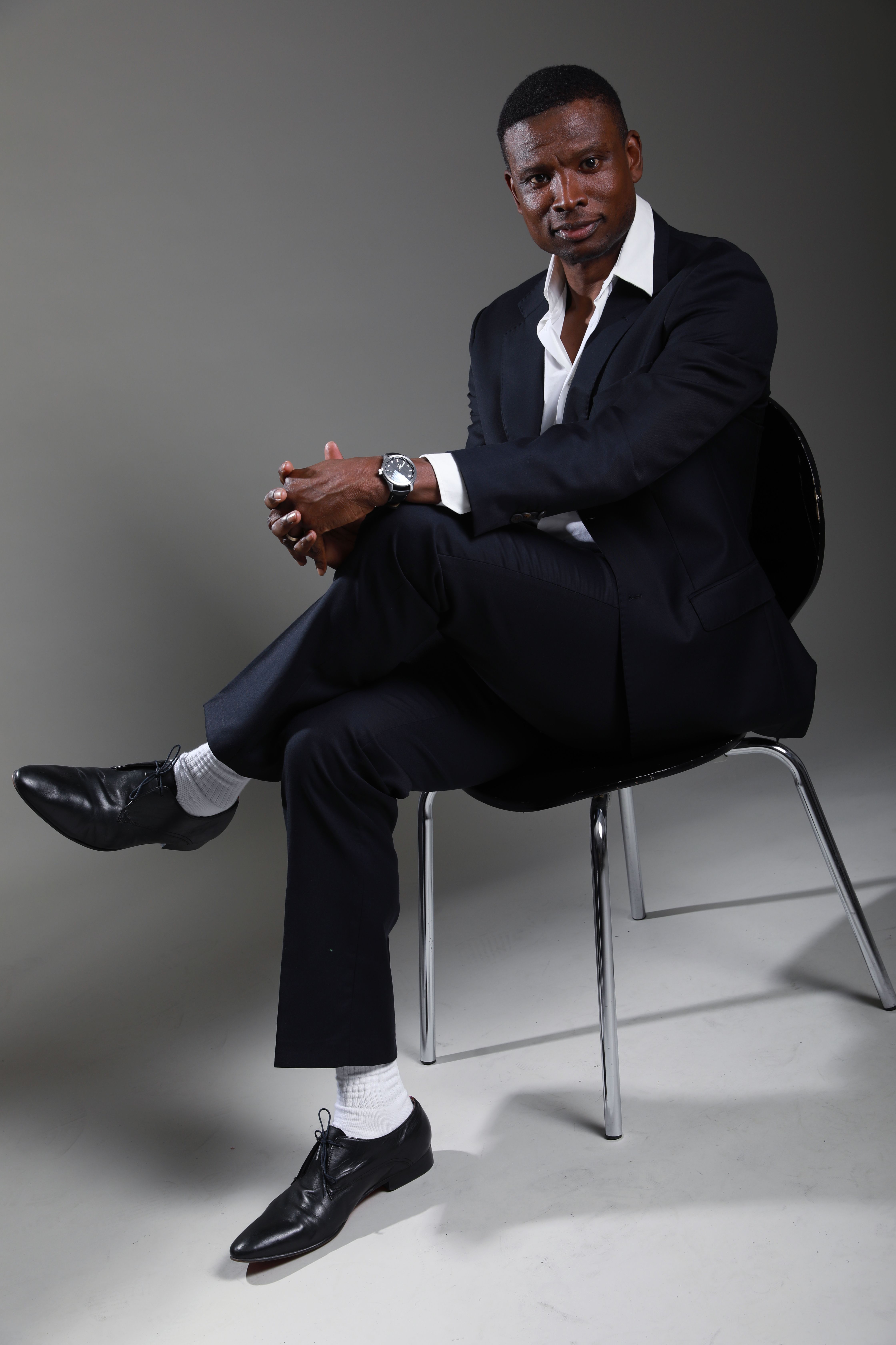 Elegant studio portrait of a man in a black suit posing confidently.