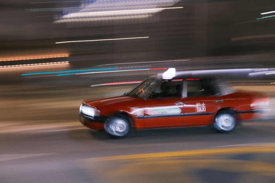 A red taxi captured in motion blur racing through the city streets at night.