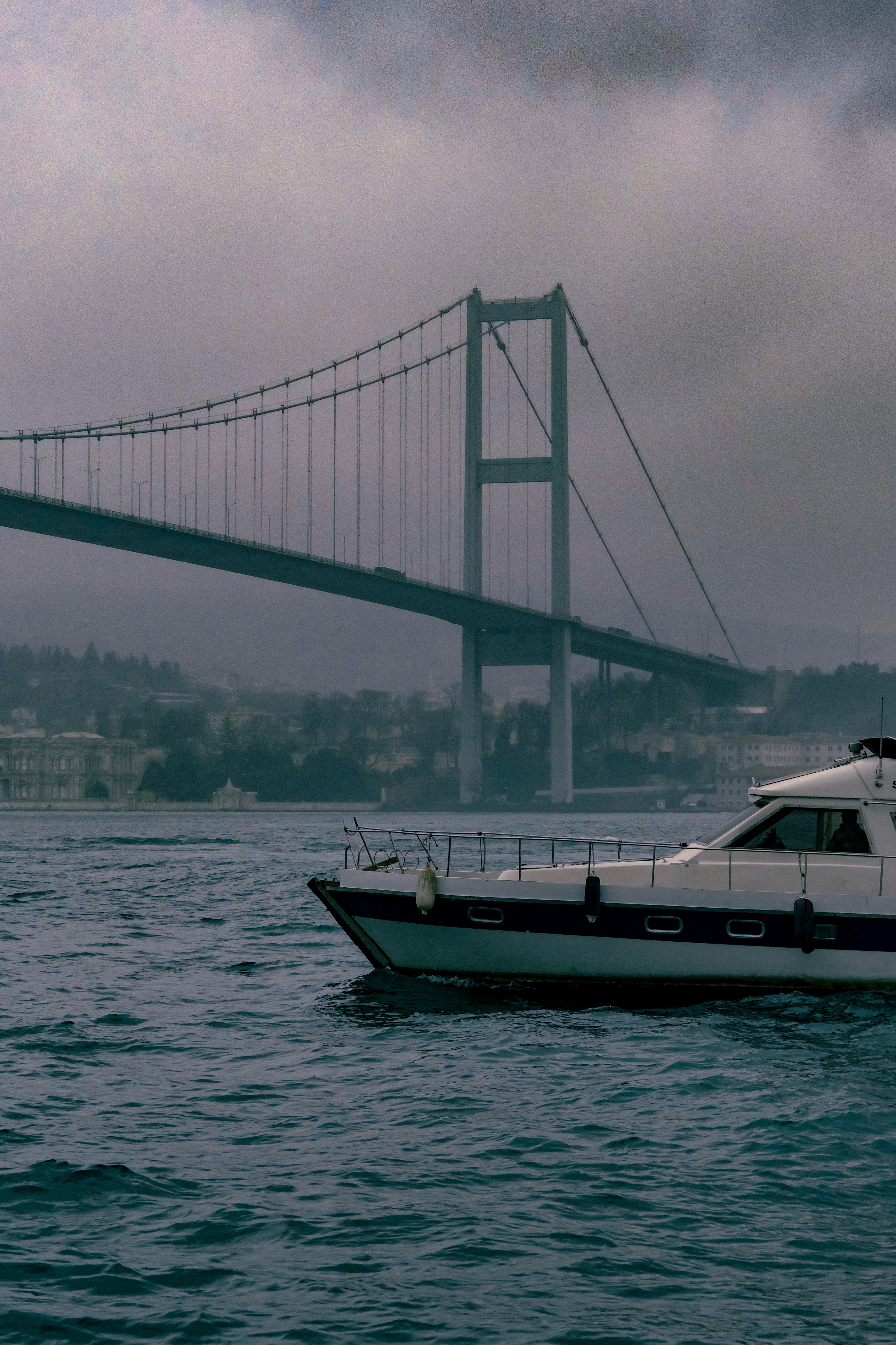 Free A yacht sails under the iconic Bosporus Bridge in Istanbul on a moody day. Stock Photo