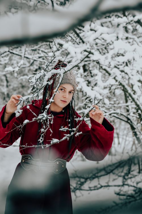 Free Portrait of a woman in red clothing, standing among snowy branches in winter. Stock Photo