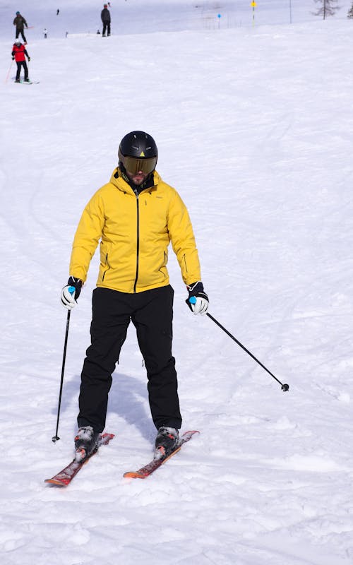 A man in a yellow jacket and black pants on skis