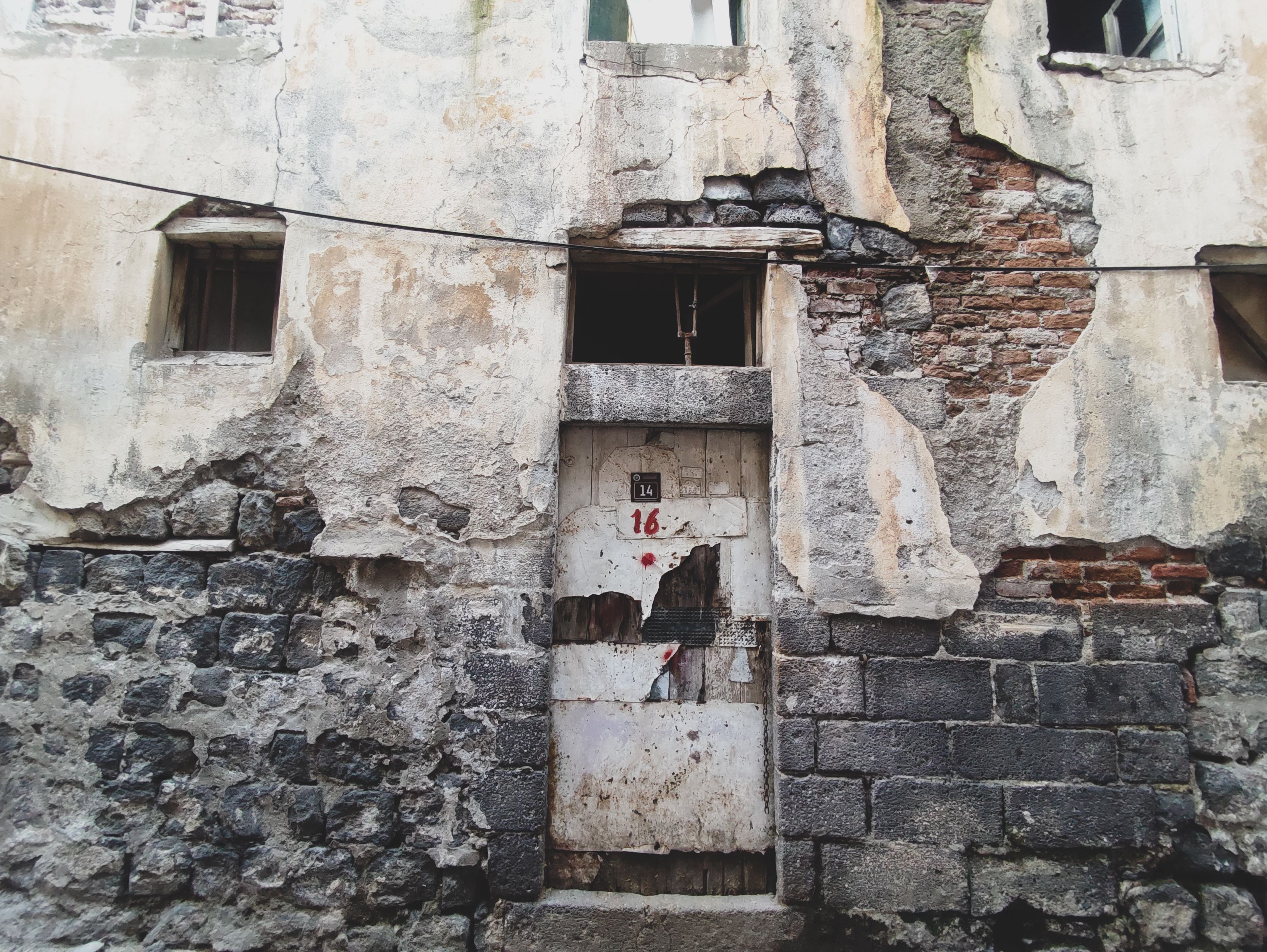 Close-up of a weathered door on a deteriorating stone building facade, showing signs of decay.