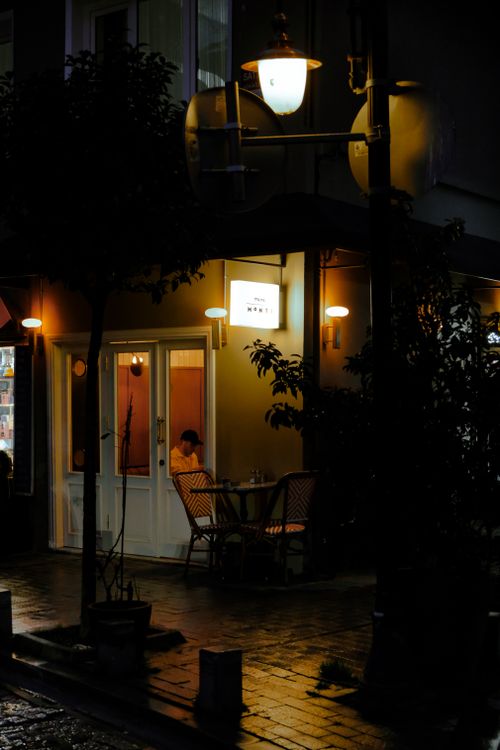 Free A person sits at an outdoor café in Beşiktaş, Istanbul, illuminated by warm street lamps on a rainy night. Stock Photo