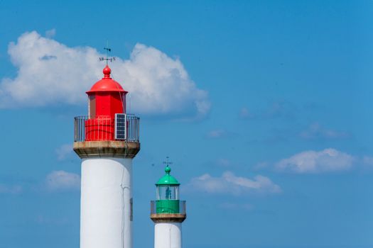 Two colorful lighthouses with a clear blue sky and fluffy clouds, showcasing maritime navigation.