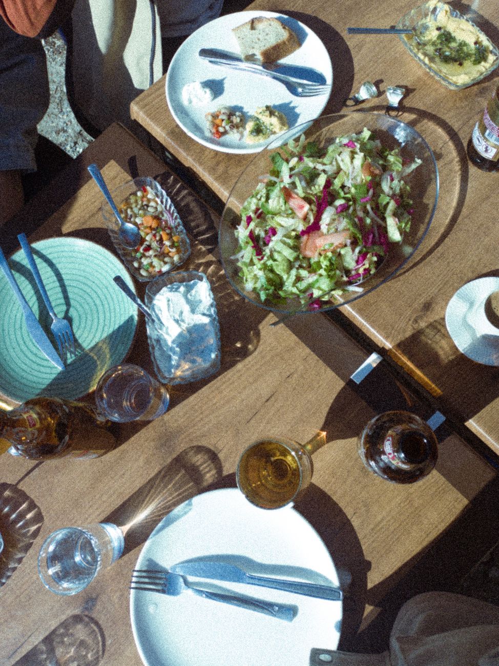 A vibrant overhead view of a lunch table featuring salads, drinks, and cutlery outdoors.