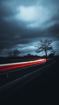 Dramatic long exposure capture of car light trails on a rural road with an overcast sky.