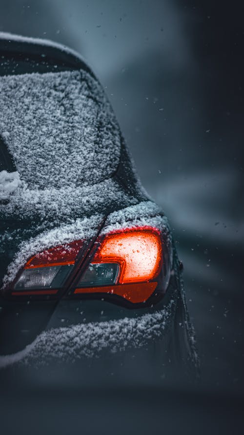 A car is covered in snow and the headlights are on