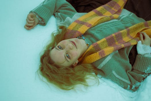 A serene woman lying on snow in winter, wearing a colorful scarf and woolen sweater.