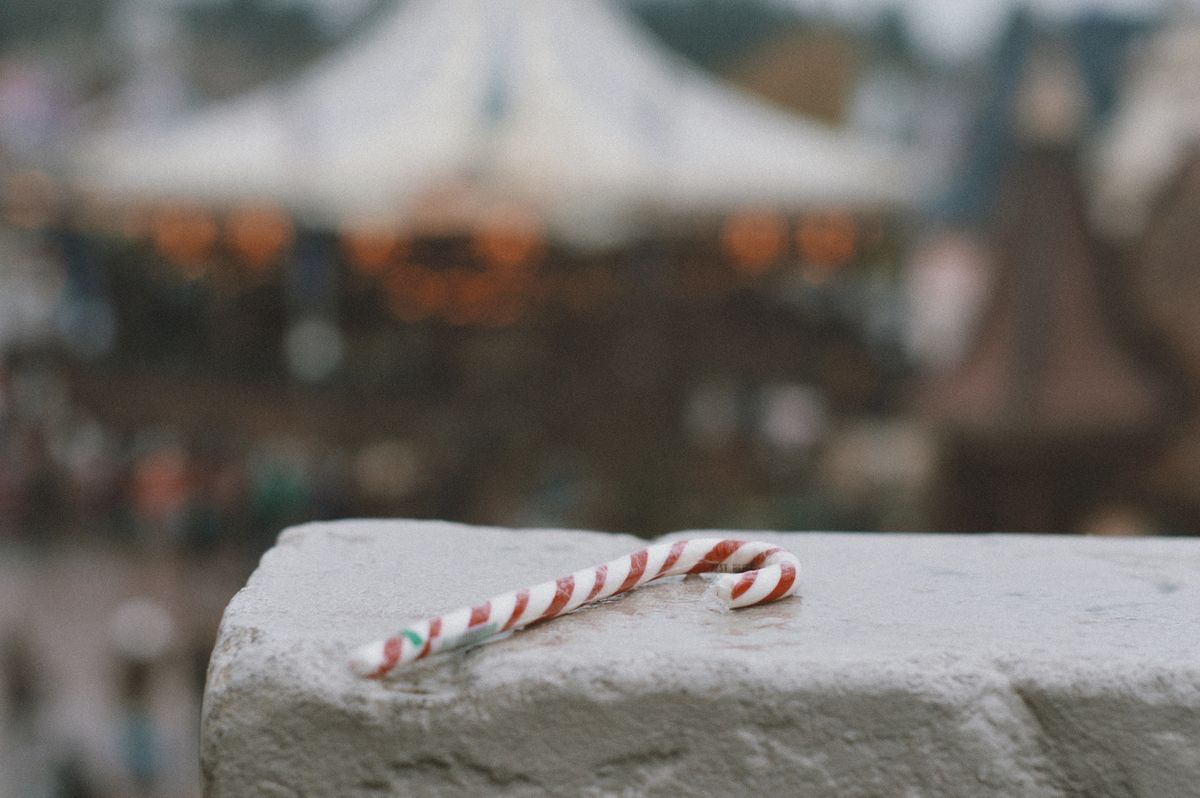 A close-up of a candy cane lying on a stone wall with a blurred city background.