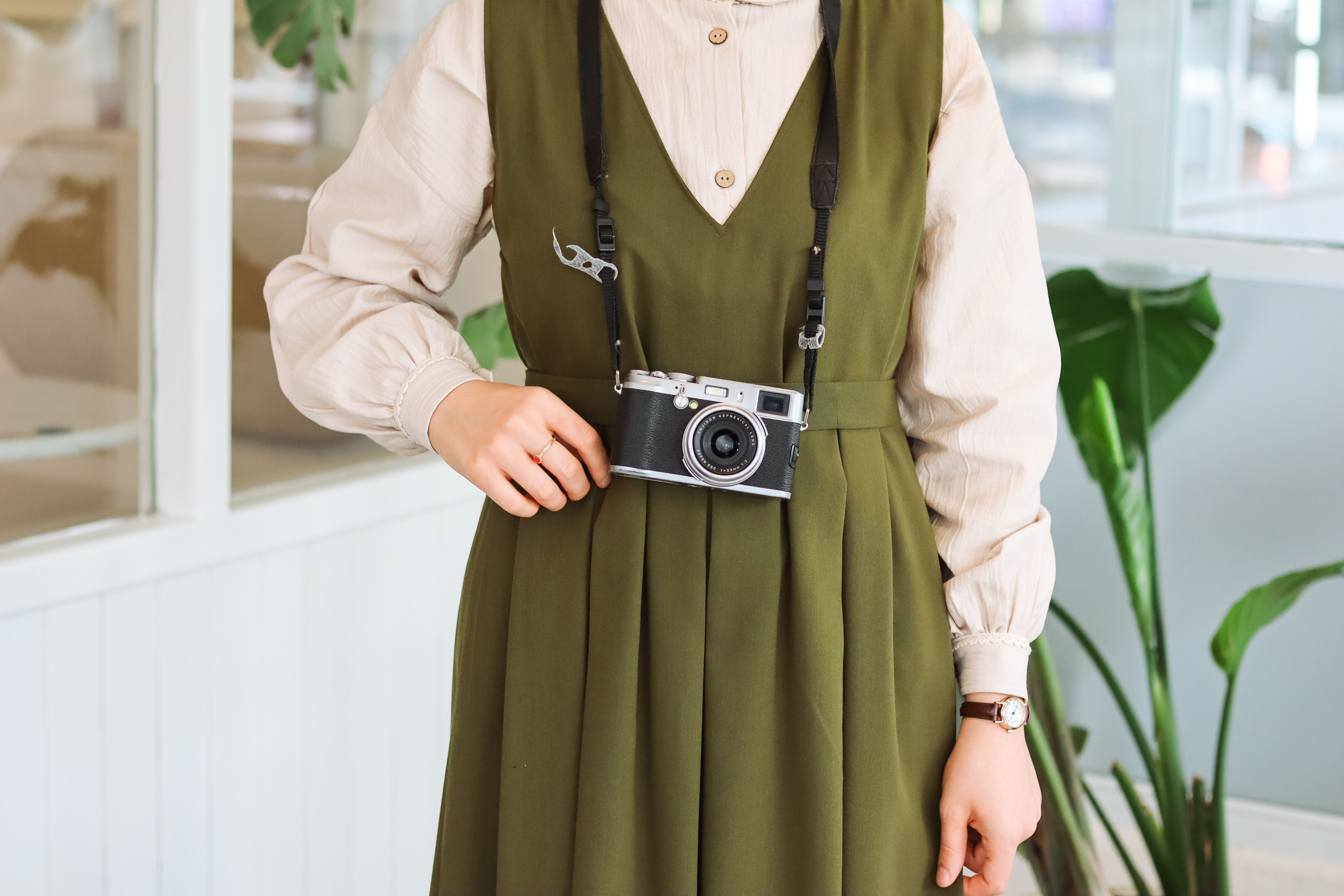 A woman in a green dress stands indoors holding a vintage camera.