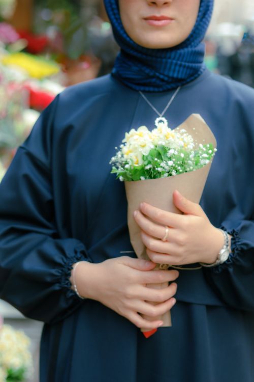 Free A woman in a navy outfit holding a small bouquet of white flowers in an urban area. Stock Photo