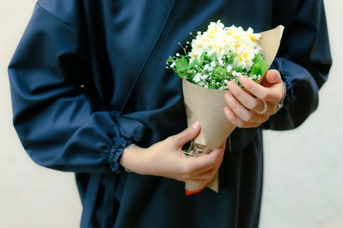 Free A woman in a blue dress holds a bouquet of yellow and white flowers. Stock Photo