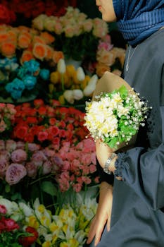 A woman in a hijab holding a beautiful floral bouquet in a vibrant florist shop.
