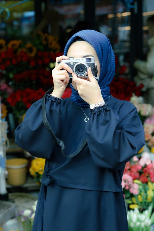 Free A woman wearing a hijab captures a photo with an analogue camera in a vibrant outdoor setting. Stock Photo