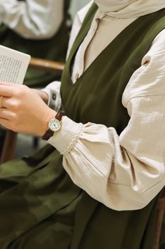 A close-up of a woman in a green dress reading, showcasing elegance and a wristwatch.