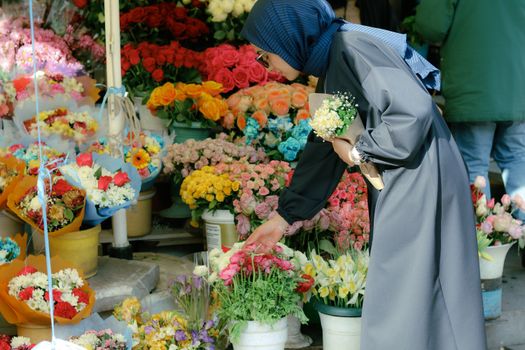 Woman in hijab choosing flowers at an outdoor market on a sunny day.