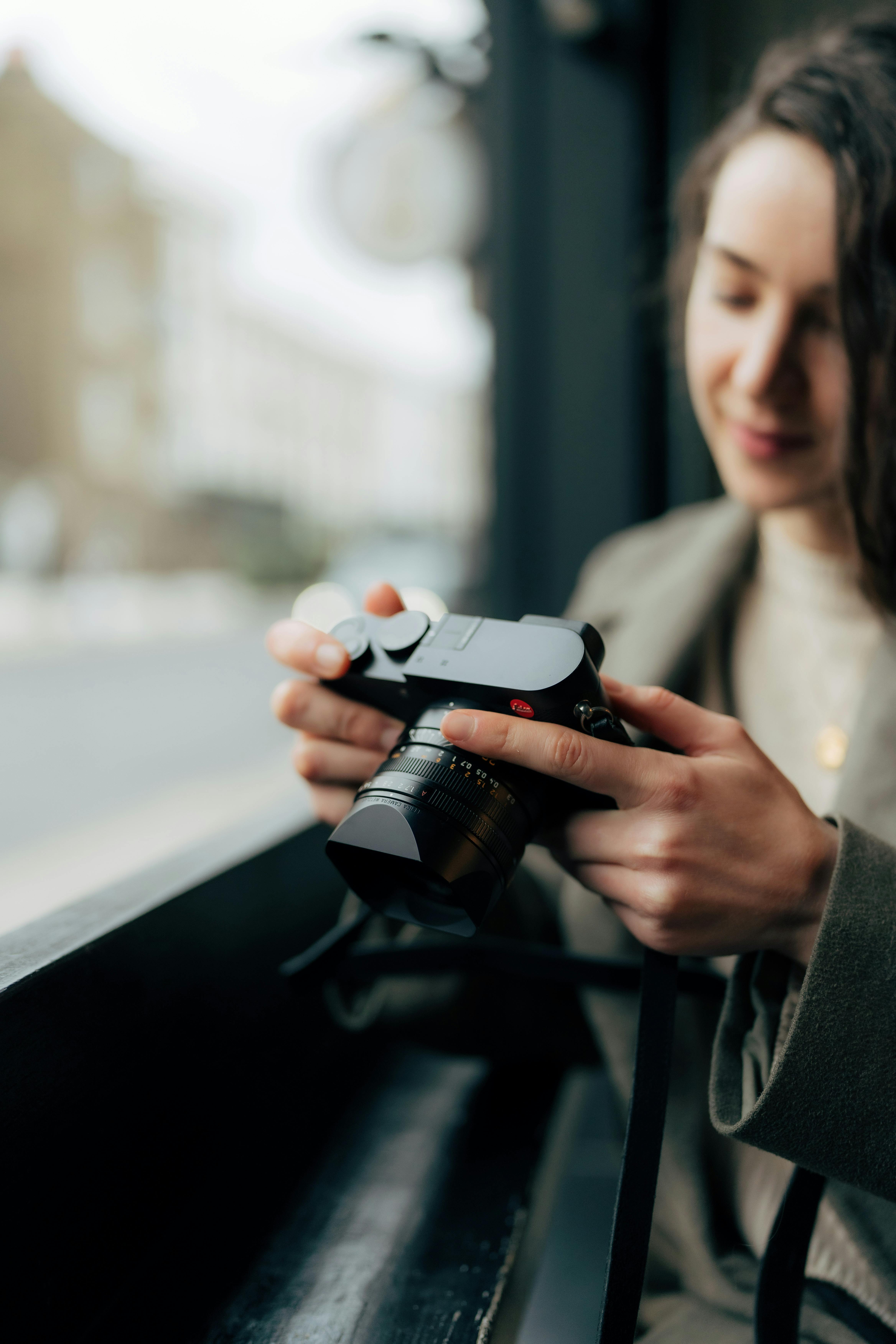 A woman holds an analogue camera by a window in a cozy urban cafe in England.