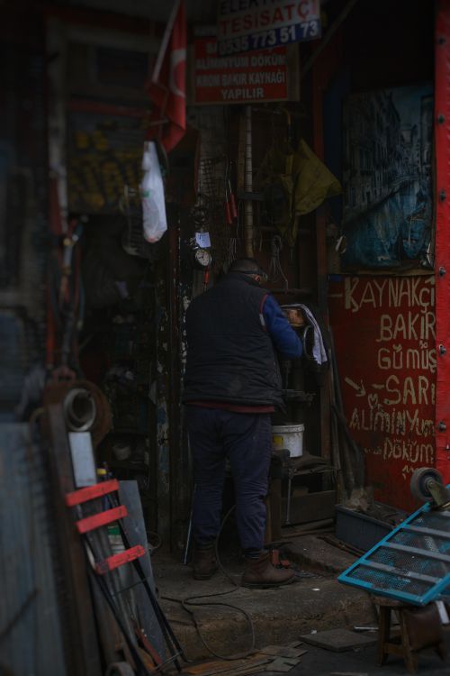 Free An elderly man stands working in an urban workshop, surrounded by tools and signs. Stock Photo