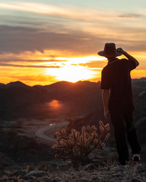 Man in Hat Standing on Hilltop at Sunset