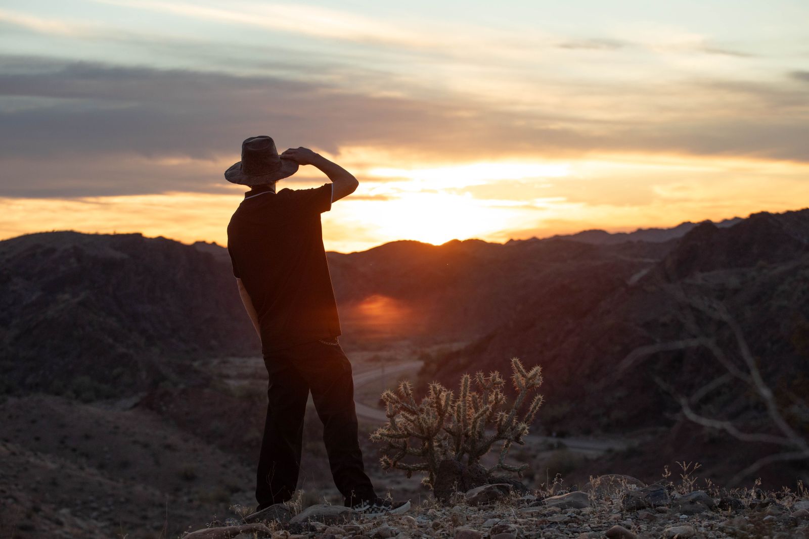 A lone traveller in a wide-brimmed hat looking out over desert hills at sunrise — photograph by Smallz ! on Pexels