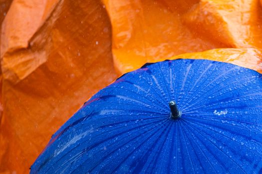 Close-up of a blue umbrella with raindrops against an orange background.