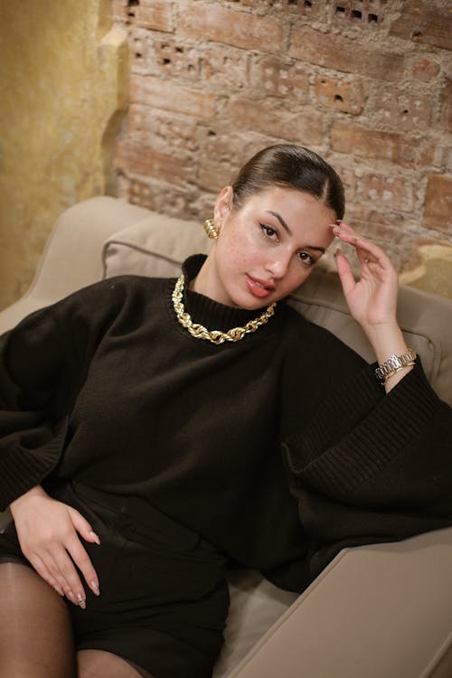 A woman in black and gold jewelry sitting on a couch