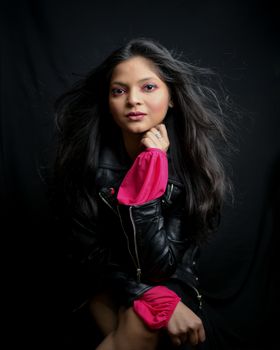 Portrait of a fashionable woman in a leather jacket with a dramatic dark background.