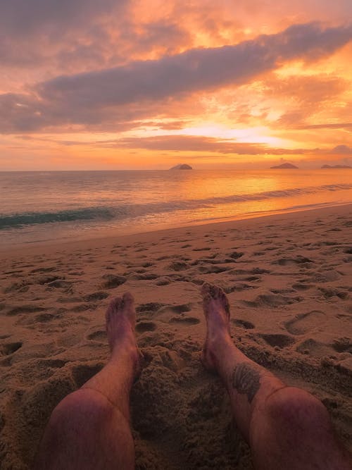 A person's feet on the beach at sunset