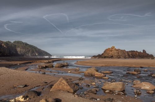 Free A serene coastal scene featuring rocks, stream, and ocean waves under a partly cloudy sky. Stock Photo