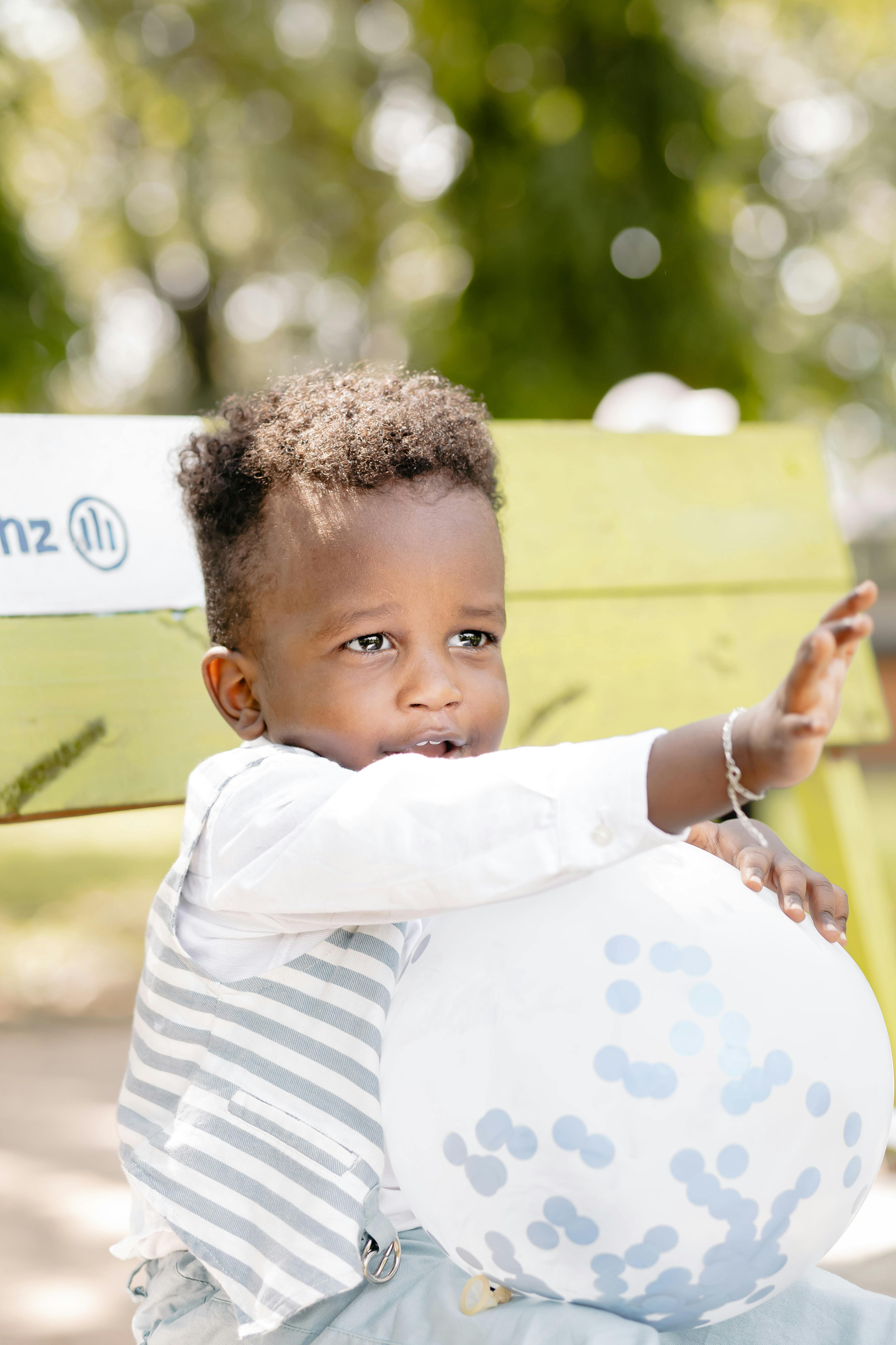 Charming portrait of a young boy holding a balloon while sitting on a park bench in the sun.
