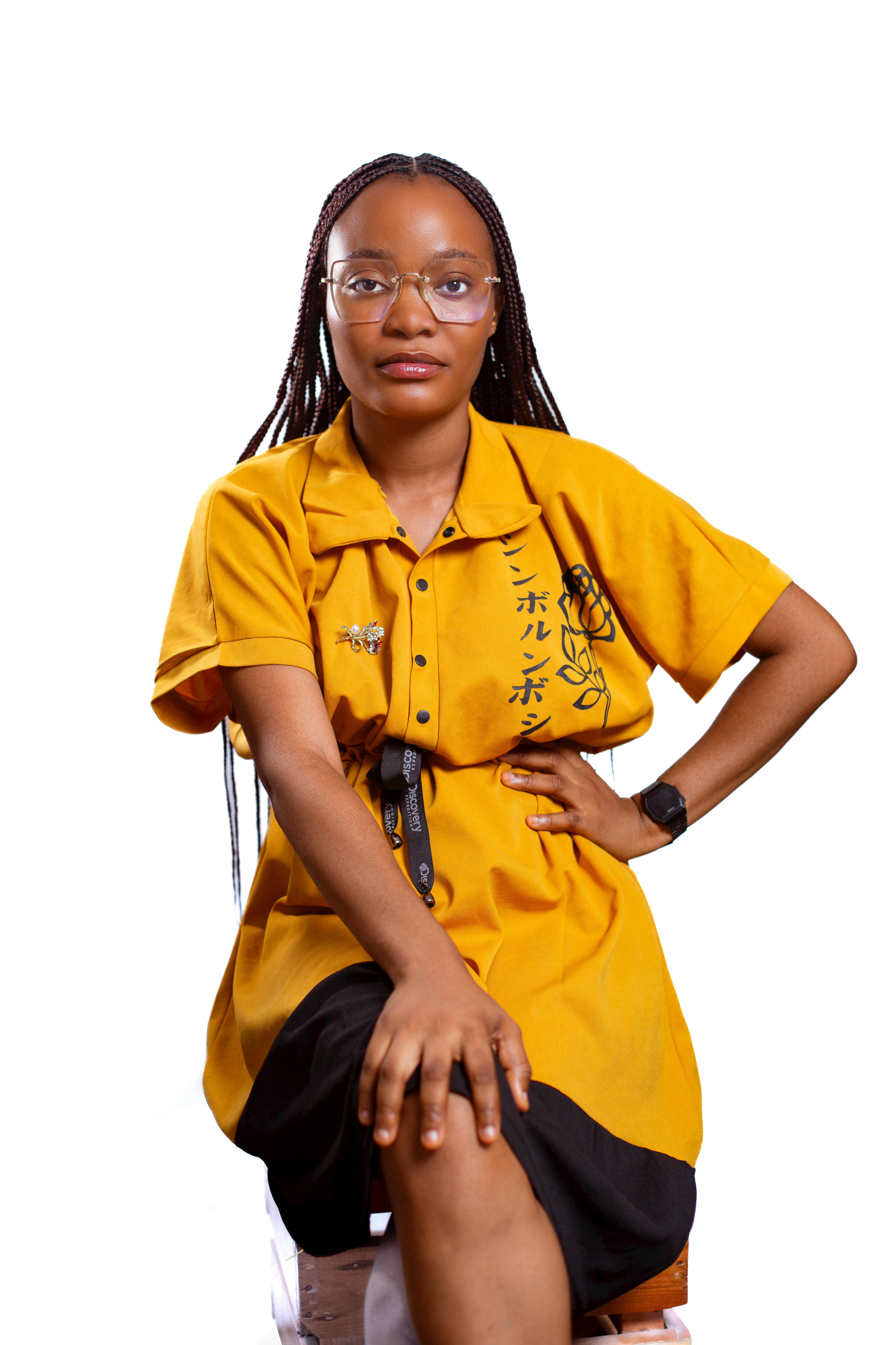 Fashionable woman in yellow dress and eyeglasses sitting confidently, studio portrait.
