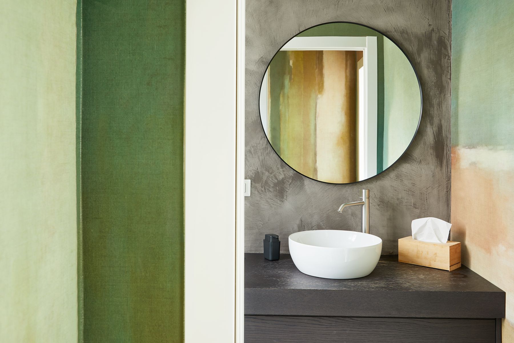 Green painted walls surrounding a vanity and round mirror