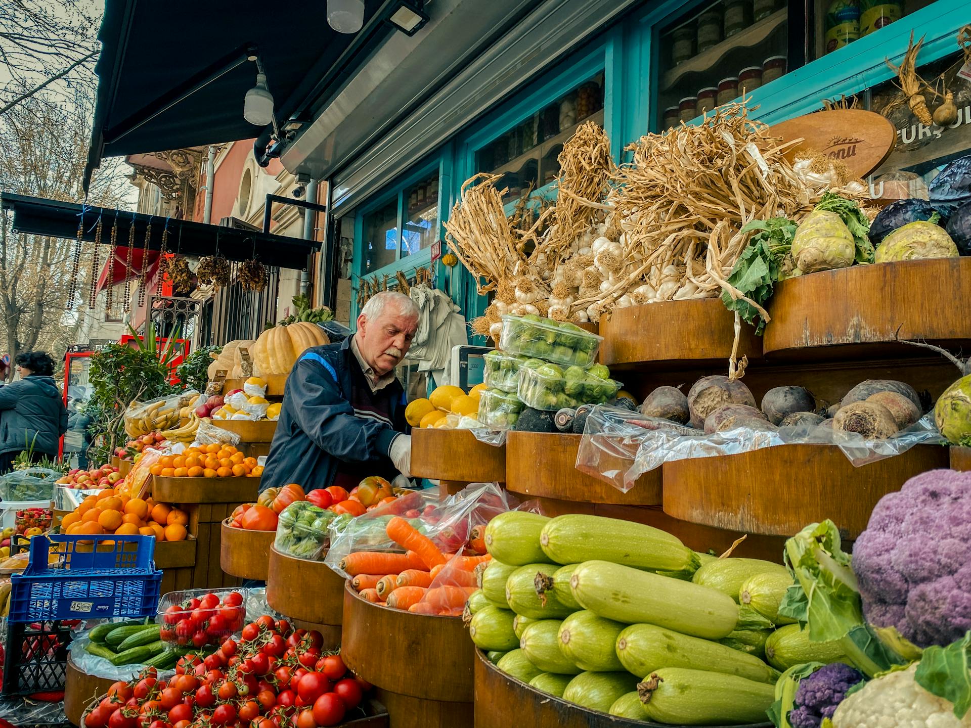 Bustling urban produce market with fresh vegetables and fruits, vendor attending to stall.