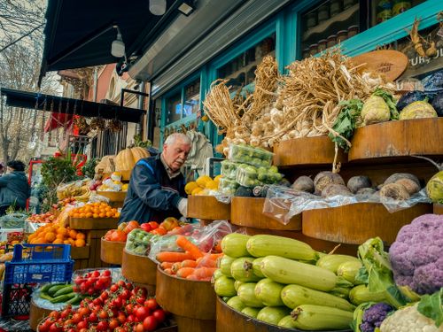 Free Bustling urban produce market with fresh vegetables and fruits, vendor attending to stall. Stock Photo