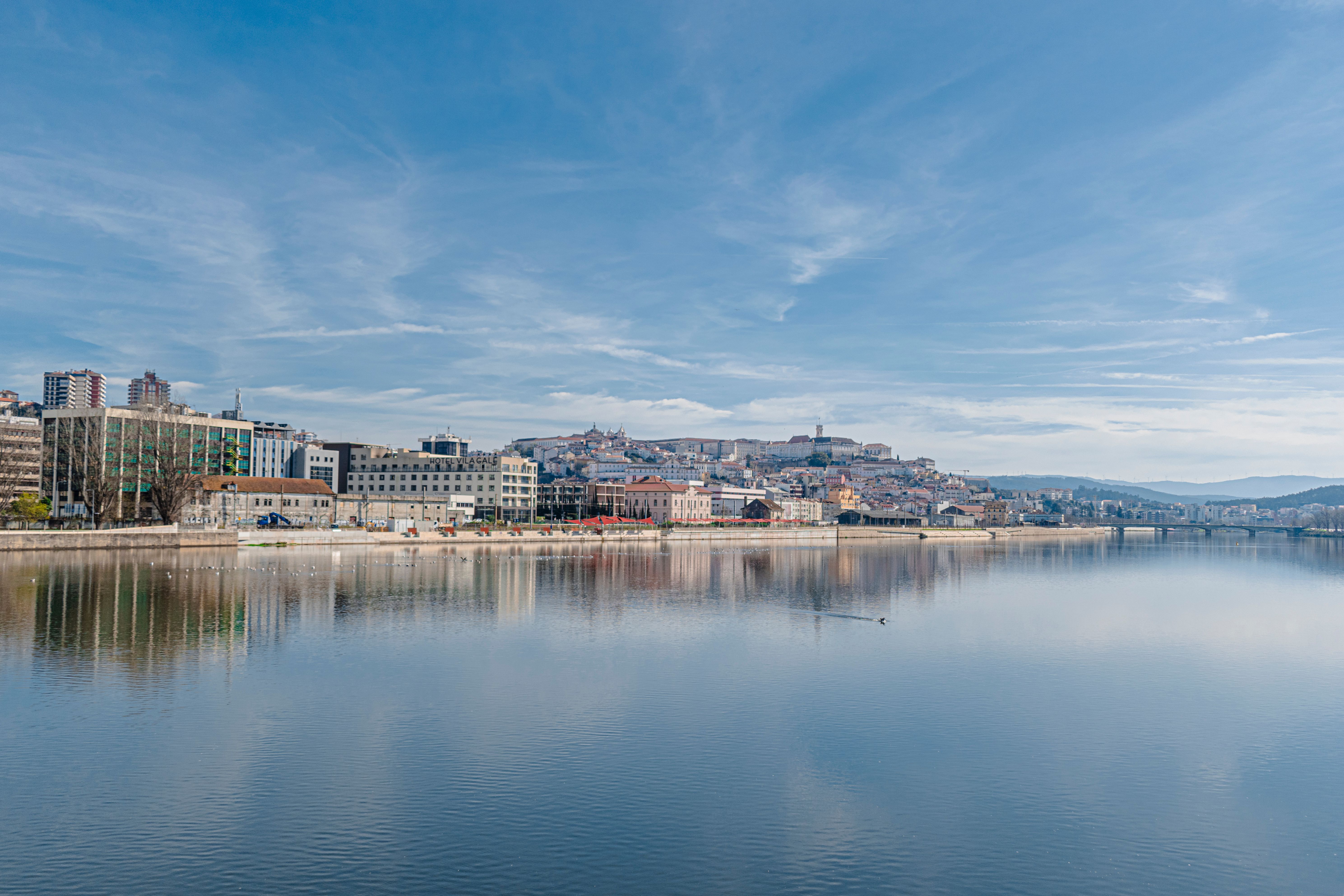 Beautiful cityscape of Coimbra with reflections in the Mondego River under a clear sky.