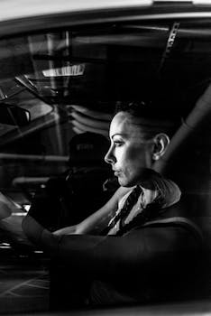 Black and white portrait of a woman sitting in a car, viewed through the window.
