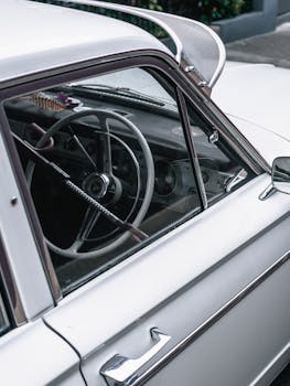 Close-up of a vintage car's interior featuring a classic steering wheel and chrome details, showcasing timeless design.