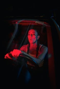 A woman driving at night with dramatic red lighting, emphasizing emotion inside a car.