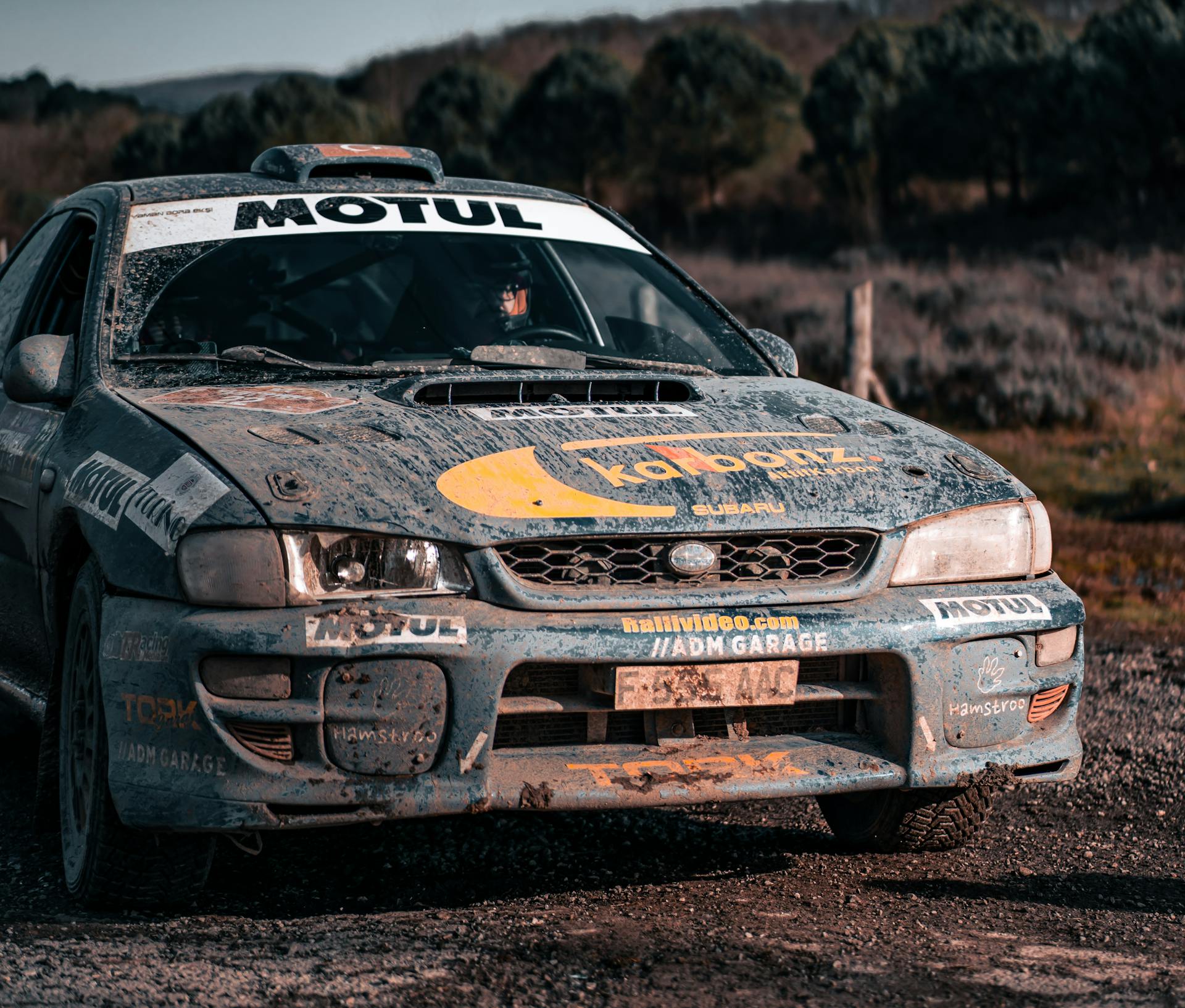 Muddy rally car showcases grit and speed on rugged outdoor racetrack under daylight.