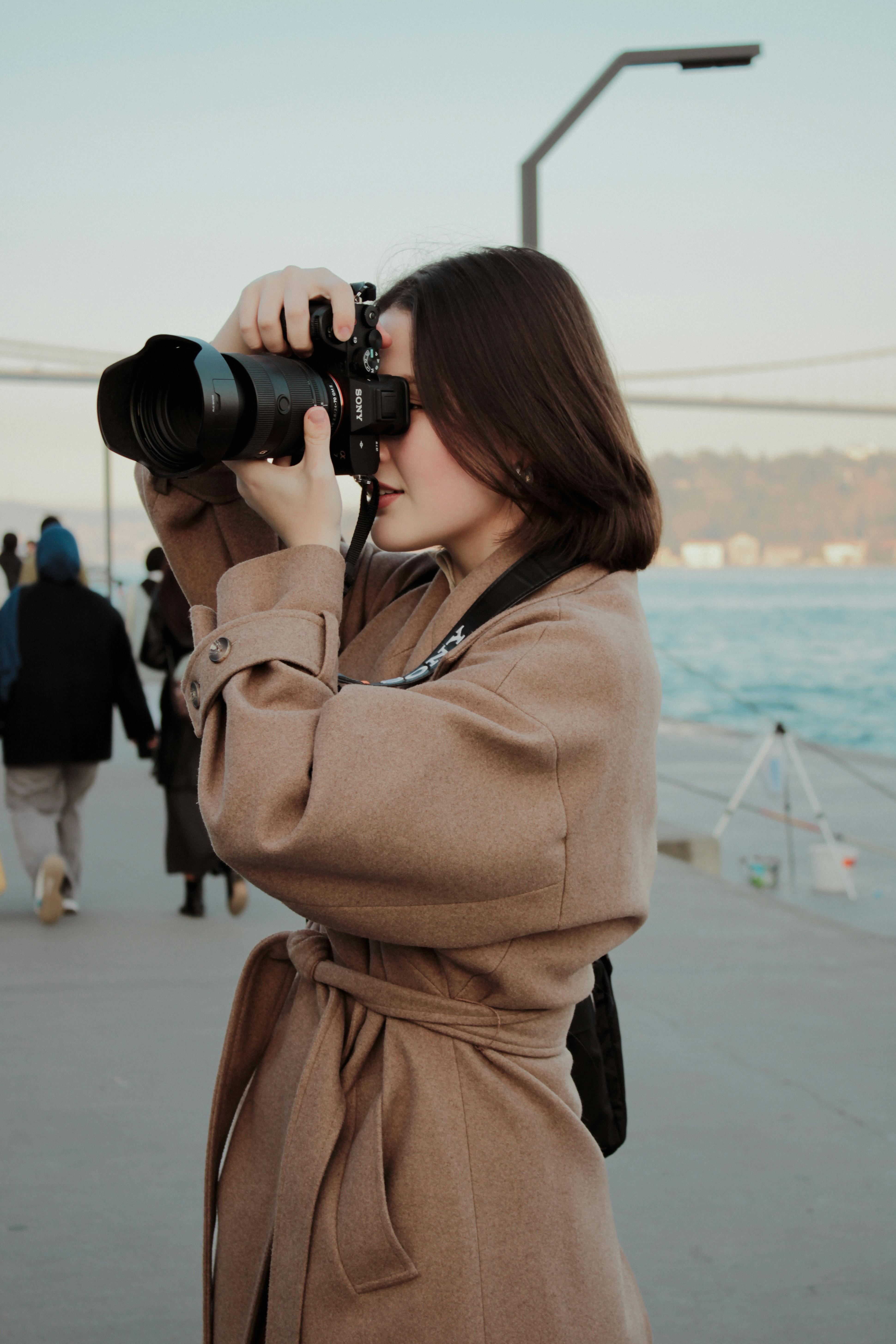 Woman taking photos near water's edge, showcasing winter fashion and outdoor photography.