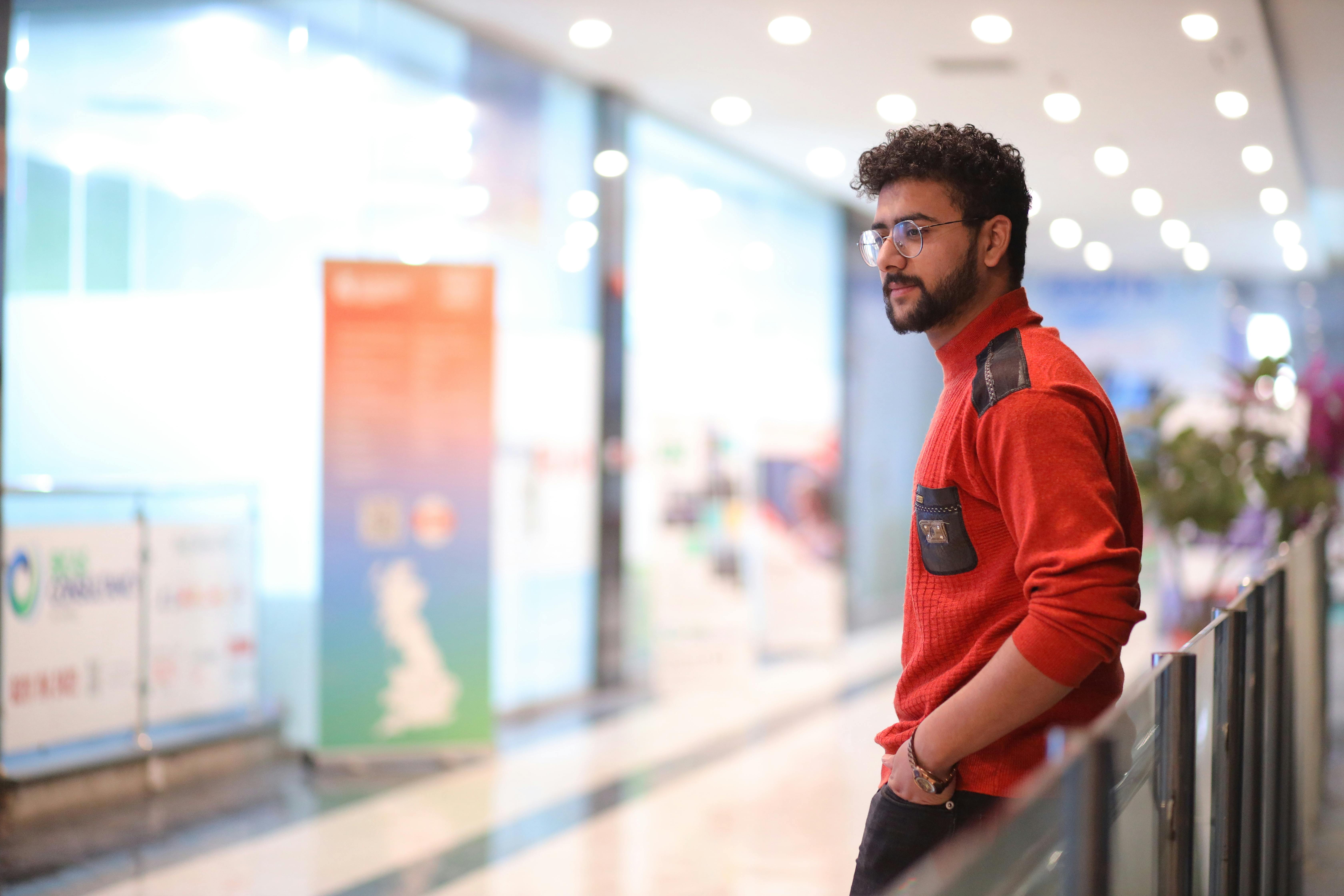 Man in red sweater standing thoughtfully at a shopping mall in Islamabad, Pakistan.