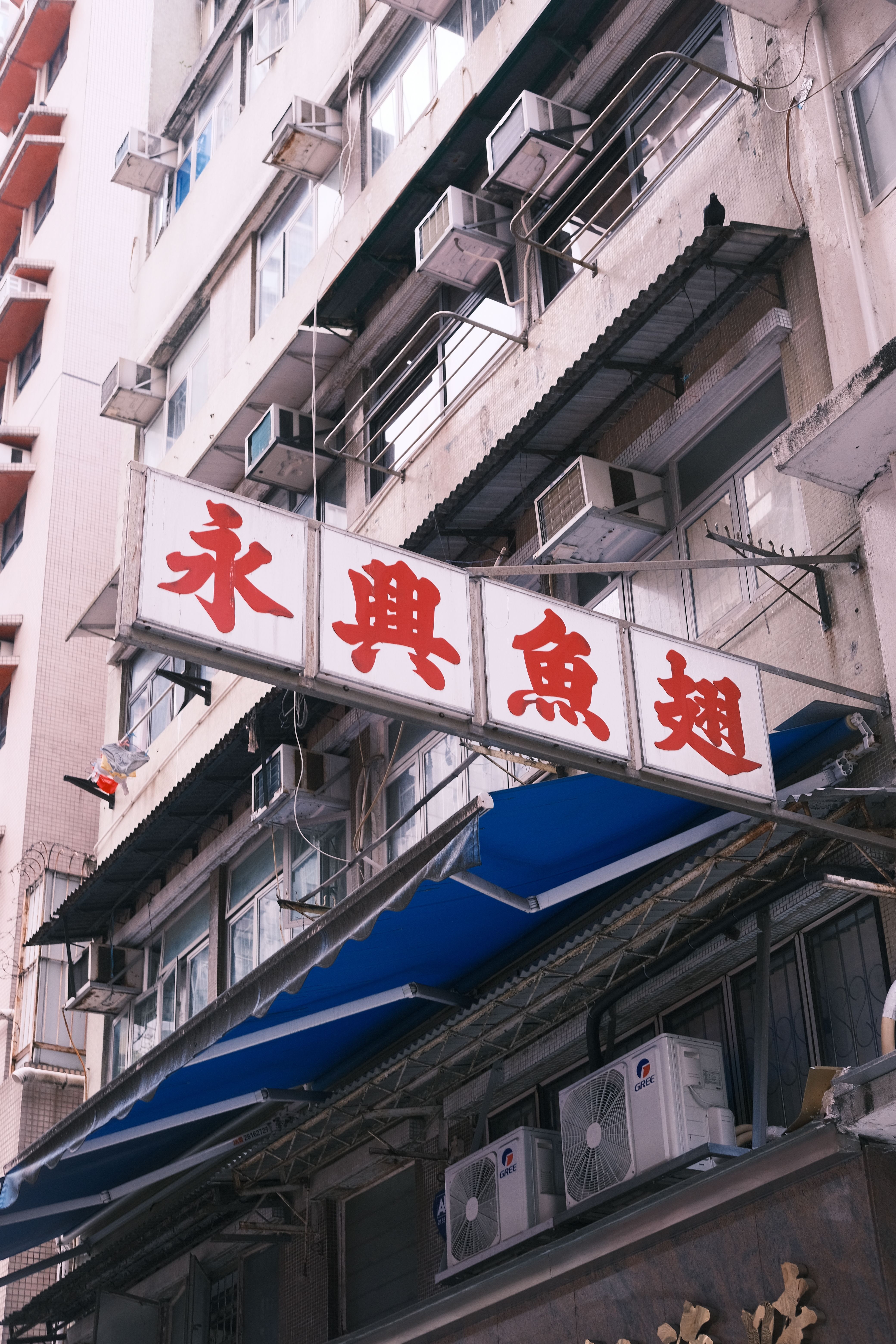 Low angle shot of a residential building featuring red Chinese signage and air conditioners on balconies.